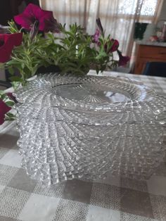 a clear glass dish sitting on top of a checkered table cloth next to pink flowers