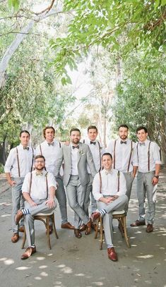 a group of men standing next to each other wearing ties and suspenders in front of trees