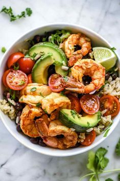 shrimp and avocado salad in a white bowl with cilantro, tomatoes, cucumber, black olives, rice