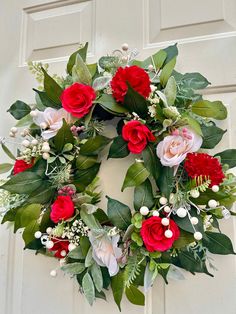 a wreath with red and white flowers hanging on a door