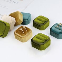 four different colored rings sitting on top of each other next to a ring box with two engagement rings in it