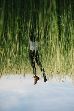 a man standing in tall grass with his feet up on the water's edge