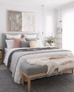 a bedroom with white walls and grey bedding, rugs on the floor, artwork above the bed