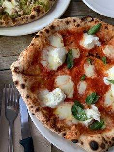 two pizzas on white plates with silverware next to them