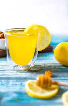 a glass filled with lemonade sitting on top of a table next to sliced lemons