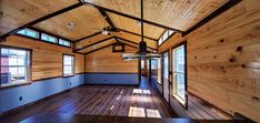 an empty room with wooden walls and ceiling fan in the center, windows on both sides