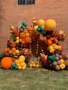 a bunch of balloons that are on the ground in front of a brick wall and grass