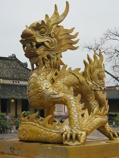 a golden dragon statue sitting on top of a wooden platform in front of a building