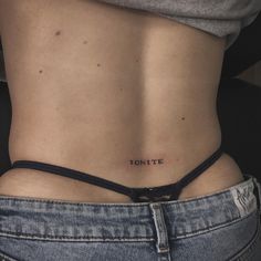 a woman's lower back with the word ignite tattooed on her left side