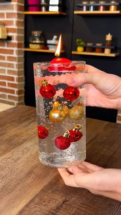 a person holding a glass filled with water and ornaments on top of a wooden table