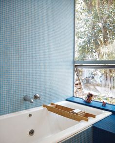 a bath tub sitting under a window next to a blue tiled wall in a bathroom