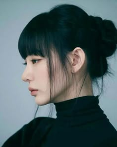 a woman with black hair wearing a black turtle neck sweater and bun hairstyle, looking off to the side