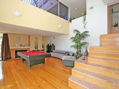 a pool table in the middle of a living room with stairs leading up to it