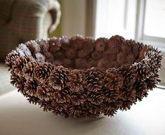 a bowl filled with pine cones sitting on top of a white table next to a chair