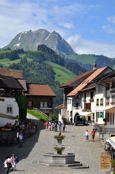 people are walking around in an old town with mountains in the background and buildings on either side