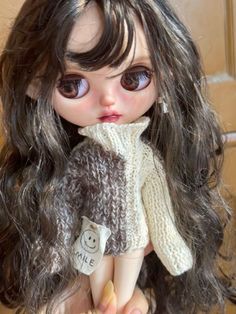 a close up of a doll with long dark hair and brown eyes wearing a sweater