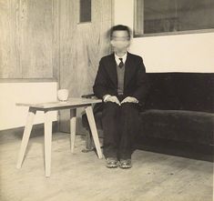 a man sitting on top of a wooden floor next to a table and couch in a living room