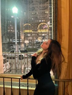 a woman standing in front of a window looking out at the street lights and buildings