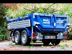 a blue dump truck parked on the side of a road in front of some trees