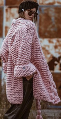 a woman is wearing a pink sweater and brown pants while standing in front of an old rusty building