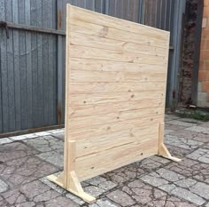 a large wooden frame sitting on top of a brick floor next to a fence and building