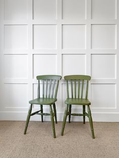 two green chairs sitting next to each other in front of a white paneled wall