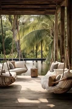 two hanging chairs on a wooden deck next to a body of water and palm trees