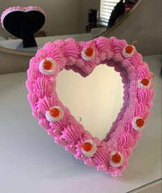 a pink heart shaped cake sitting on top of a white counter next to a mirror