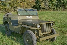 an old green jeep is parked in the grass