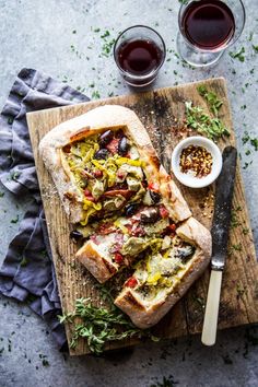 a wooden cutting board topped with bread and olives next to two glasses of wine