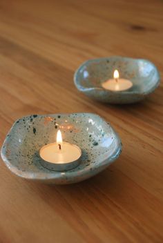 two tea lights sitting on top of a wooden table next to each other in small bowls