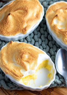 four baked desserts in white bowls on a wooden tray with silverware and spoon