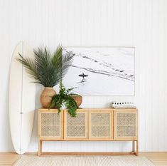 a white surfboard sitting on top of a wooden shelf next to a plant and a painting