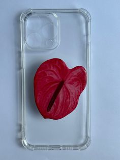 a phone case with a red heart shaped object on the front and back sides, sitting on a white surface