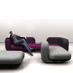 a man sitting on top of a couch in front of a white wall with purple and grey furniture