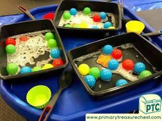 two trays filled with different colored candies on top of a blue table next to utensils