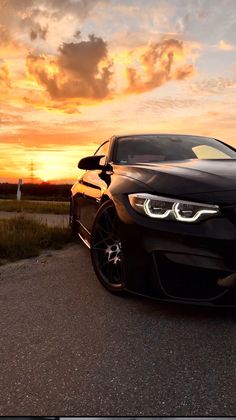 a black car is parked on the side of the road at sunset with clouds in the background