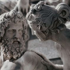 two statues of men with beards and hair, one is looking at the other