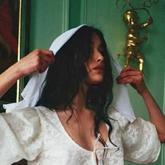 a woman wearing a white wedding dress and holding a gold object in her hand while standing next to a green door