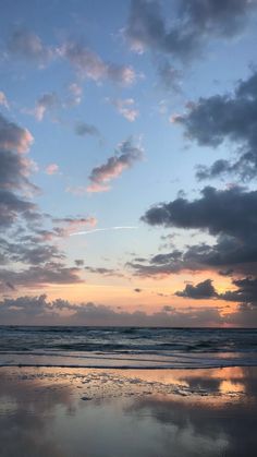 the sky is reflected in the wet sand on the beach as the sun goes down