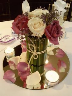 a vase filled with white and pink flowers on top of a glass table topped with candles