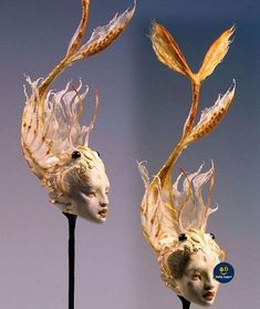 two masks with long hair on top of each other, one is white and the other has yellow feathers