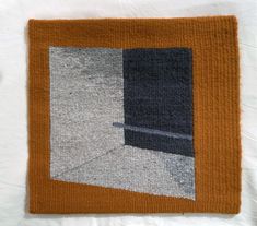 an orange and grey rug on top of a white sheet with a black square in the middle