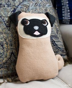 a stuffed pug sitting on top of a couch next to a blue and white pillow