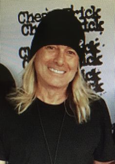 a woman with blonde hair wearing a black beanie and smiling at the camera while standing in front of a screen