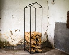 a stack of firewood in a cage next to a wall with peeling paint on it