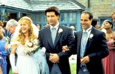 two men and a woman are walking down the aisle with their wedding party in the background