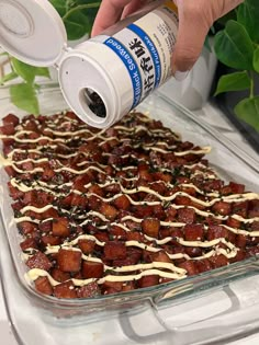 a person pouring sauce on top of a dessert in a glass baking dish with white icing