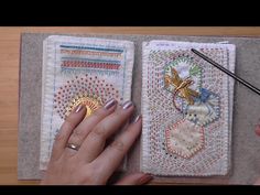 a woman's hand is holding an open book with various designs on it and a needle in the middle