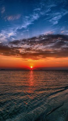 the sun is setting over the ocean with clouds in the sky and water on the beach